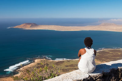 Rear view of woman sitting on stone wall against sea