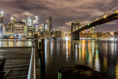 Illuminated buildings by river against sky in city at night