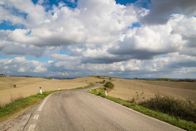 Empty road amidst field against sky