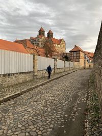 Man walking on footpath by building against sky