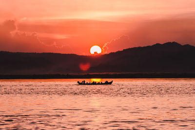 Silhouette boat in sea against orange sky