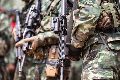 Midsection of army soldiers with rifles standing outdoors