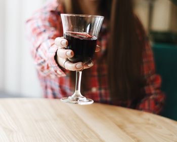 Midsection of woman holding red wine on table