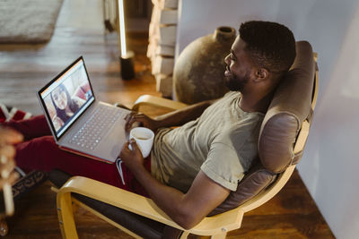 Smiling man doing video call with woman through laptop while sitting on chair at home