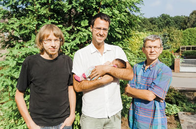 Portrait of men with baby standing by tree outdoors