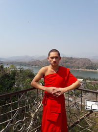 Portrait of young man standing on railing against sky