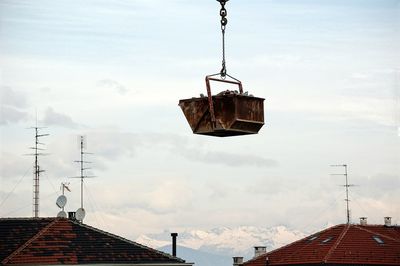 Crane hanging on roof of house against sky