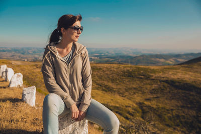 Mid adult woman wearing sunglasses sitting on rock against blue sky