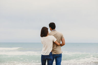 Rear view of friends standing at beach against sky