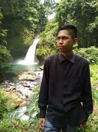 Young man standing by waterfall in forest