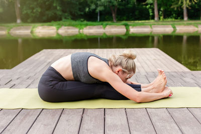 A woman by a pond in the park does yoga, doing stretching.