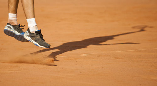 Low section of tennis player jumping while playing on ground