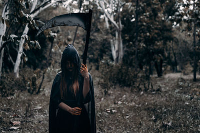 Young woman holding weapon at forest during halloween 