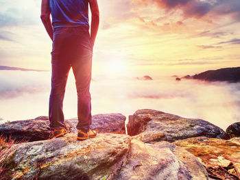 Sports figure man wearing outoor clothes and boots on rock in sunny fall day with hands in pocket