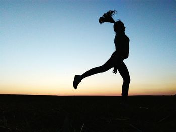 Silhouette man climbing on field against clear sky during sunset