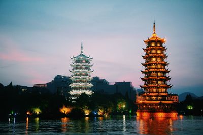 Pagodas by river against sky in city at dusk