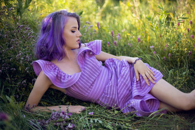 Teenage girl with dyed purple hair and a nose piercing in the grass  in a short dress