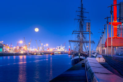 Sailboats moored at harbor against sky at night