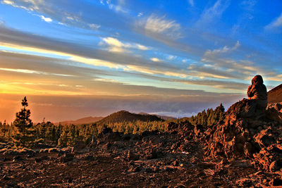 Woman on rock against sky during sunset