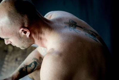 High angle view of shirtless shaved head man with tattoo sitting indoors