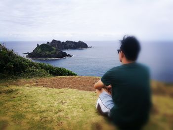 Rear view of man sitting on shore against sky