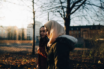 Side view of young female muslim friends walking in city during sunset