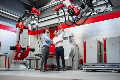 Male engineer explaining robotic arm to colleague in factory