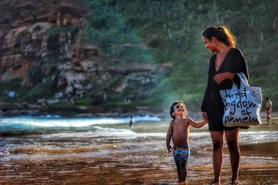 Mother with son standing at beach against mountain