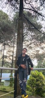 Portrait of young man standing against trees in forest