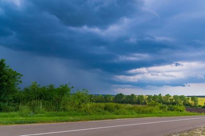 Road by trees against storm clouds