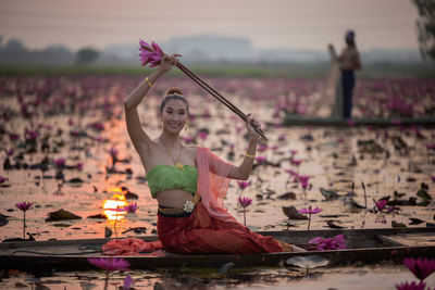 Portrait of smiling young woman holding water lilies in boat on lake