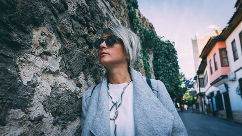 Low angle view of woman looking away while standing by stone wall