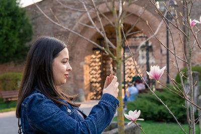 Woman using mobile phone by bare trees in city