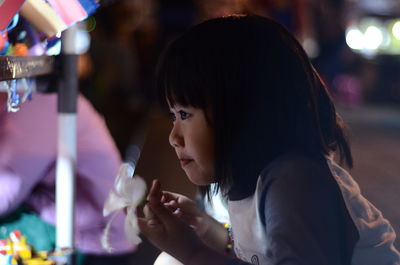 Cute girl looking away while standing by railing at night