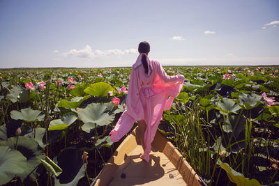 Portrait brunette woman  in a pink dress stands on a boat in the river among the lotuses in summer