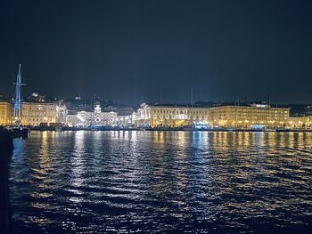Illuminated buildings by river against sky at night