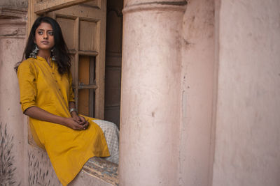 Young woman looking away while sitting on wall