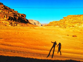 Shadow of people on land against clear blue sky