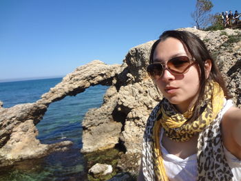 Portrait of young woman by sunglasses against sea against clear sky