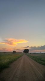 Empty road amidst field against sky during sunset