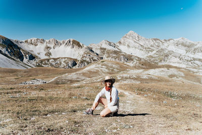 Rear view of woman sitting on mountain against sky