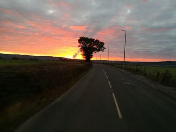 Road amidst trees against dramatic sky