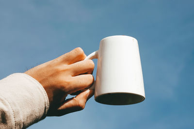 Midsection of person holding white against blue sky