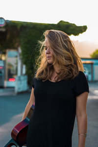 Young woman holding guitar while standing outdoors