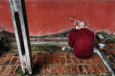 Rear view of man sitting on red wall