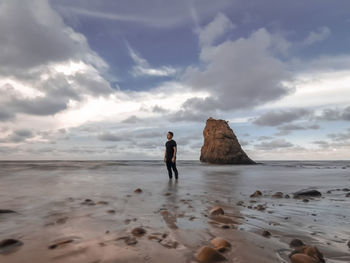 Full length of man standing on rock at beach against sky