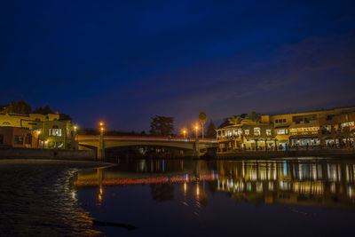 Illuminated buildings by river against sky at night