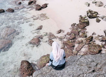 Rear view of woman sitting on rock by sea