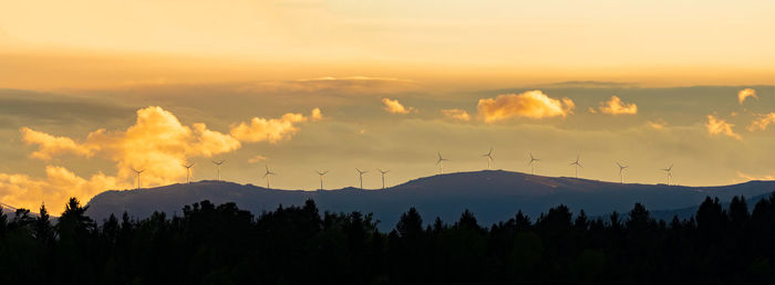 Windmills at sunset against orange sky in austria. panorama of wind turbines