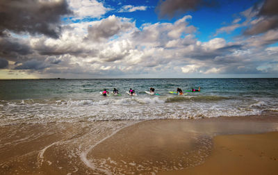 Friends surfboarding on sea against sky